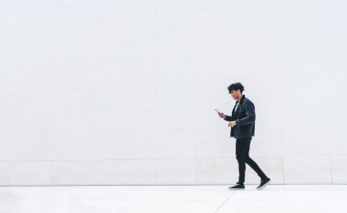 Modern stil gülümseme yan görünümü memnun genç Afrikalı Afrikalı Amerikalı adam günışığında şehir caddesinde yürürken tablet üzerinde gezinen günlük kıyafet