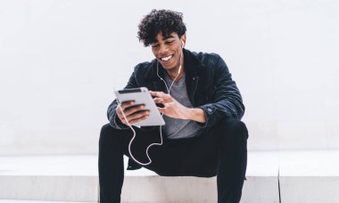 Gülümseyen erkek blogcu internet sitelerinde kulaklıkla komik filmler seyrediyor dokunmatik ped üzerinden hipster adam fotokopi alanına yakın müzik dinliyor ve dijital tabletle son haberleri okuyor.
