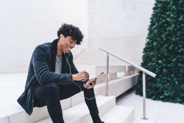 Siyah elbiseli, siyah elbiseli, tablete mesaj atan ve ekrana bakan genç, Afro-Amerikan erkek öğrencinin yan görüntüsü.