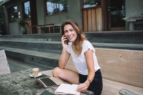 Jovem Empresária Alegre Conversando Smartphone Fazendo Anotações Enquanto Trabalhava Laptop — Fotografia de Stock