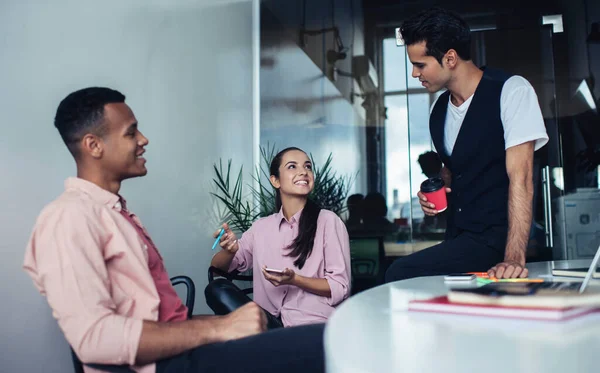 Successful business marketers sitting at desktop in coworking space and laughing during working time discussing collaboration and teamwork, happy crew of analytic experts rejoicing indoors