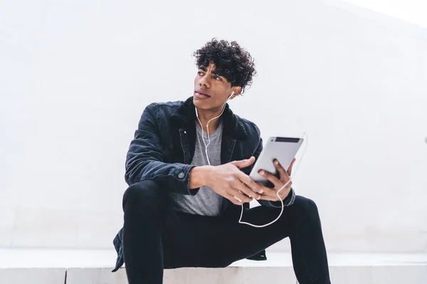 Młody Afroamerykanin Zamyślony Student Czarnych Ubraniach Siedzi Tabletem Słuchając Muzyki — Zdjęcie stockowe