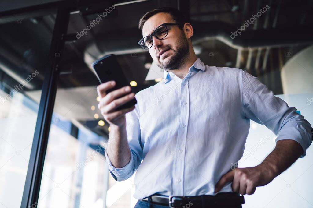 Puzzled male professional boss reading message while receiving mobile email for solving corporate problems in mobile cell mode, confused financial expert checking money exchange on trade website