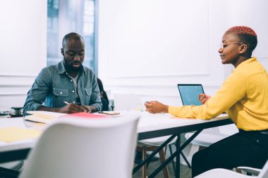 Afrikalı Amerikalı düşünceli işçiler ofis masasının etrafındaki şirketin pazarlama stratejisi hakkında konuşurken evrak işleriyle ve not almakla meşguller.