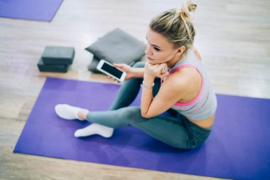 Spor kıyafetleri içinde ince, düşünceli bir sarışının spor minderinin üzerinde oturduğu yerden.