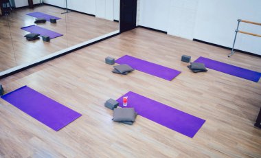 Kahverengi lamine zeminde mor yoga minderleri olan ve duvardaki büyük aynaya yansıyan boş spor salonundan.