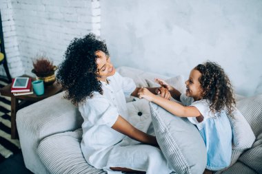 Yukardan bakıldığında, neşeli, pozitif kıvırcık anne ve kızının yastıkla oynayıp birbirlerine baktıkları görülüyor.