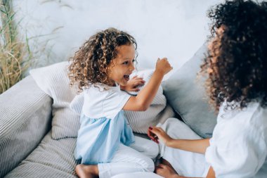 Oturma odasında boş zamanlarımızda annesiyle kanepede oynayan neşeli, kıvırcık kızın yukarıdan bakışı.