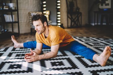 Kırmızı tişörtlü, mavi pantolonlu, elleri beyaz ve siyah halıya yaslanmış genç, güçlü, esnek bir erkek. 