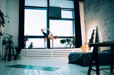 Spor giysileri içinde çalışan, el pencerede ayakta duran ve eve bakan çok çalışan kadınların yan görüntüsü.