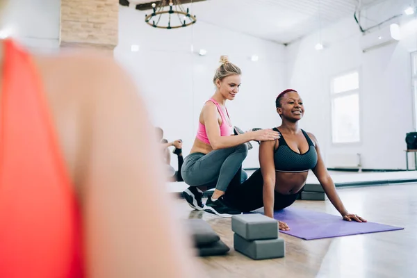 Crop multiracial yoga women group in fitness studio leaning on hands and knees on gym mats raising torsos under supervision of instructor