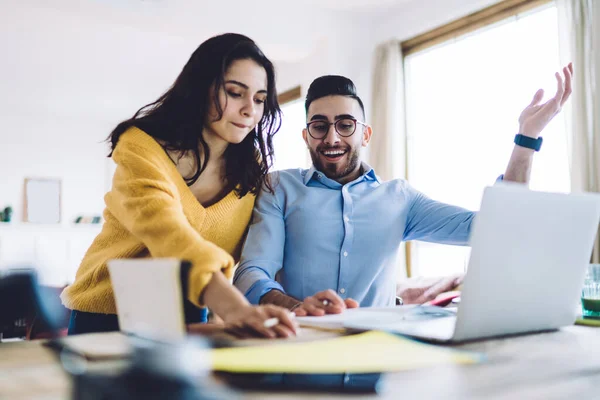 Casual thoughtful remote workers thinking about project, woman checking notes with cheerful man fling up hand while thinking about solutions at home