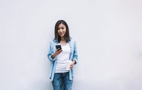 Молодая Веселая Азиатка Синей Рубашке Джинсах Джинсах Опирающаяся Стену Смартфоном — стоковое фото