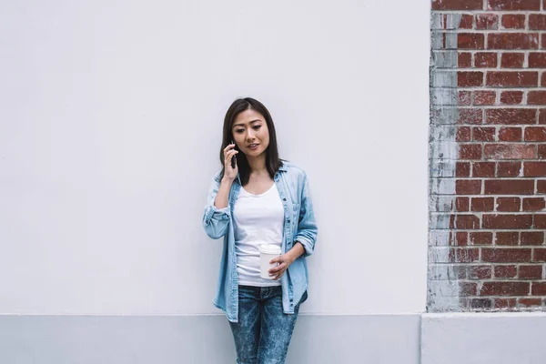 Молодая Красивая Азиатка Голубой Одежде Разговаривает Телефону Опираясь Стену Чашкой — стоковое фото