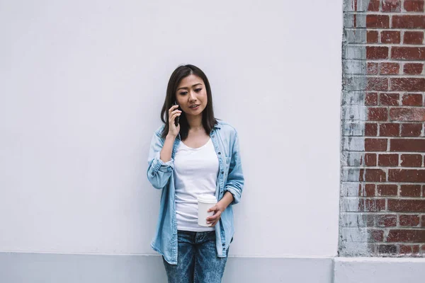 Красивая Азиатка Голубой Одежде Разговаривает Телефону Опираясь Стену Чашкой Кофе — стоковое фото