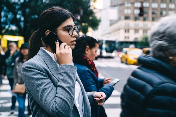 Side view of female entrepreneur calling to operator service for consultancy about roaming internet connection for future business trip, Latino trader in optical glasses walking at urban setting