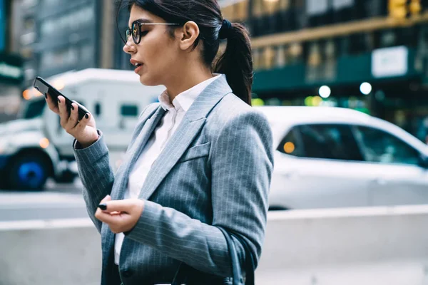 戴眼镜 穿着正装 手持智能手机站在街上进行电话交谈的女企业家的侧面形象 — 图库照片