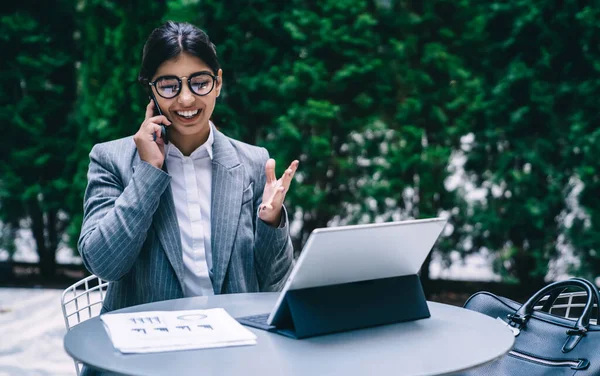 Happy female accountant in optical eyewear for vision protection enjoying positive smartphone conversation with 4g roaming connection for discussing good news about developing startup project