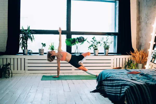 在明亮舒适的带有木制地板和绿色的公寓里 穿着运动服锻炼 躺在瑜伽垫上的漂亮的女运动员 — 图库照片