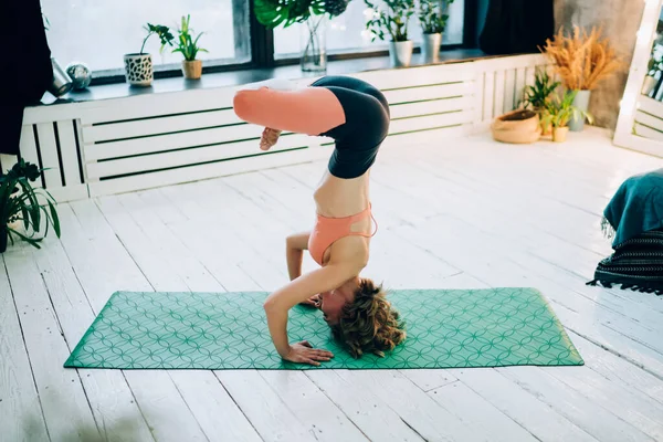 身材苗条的女性穿着运动服在莲花头架上锻炼瑜伽 双腿交叉 坐在现代房间的绿色垫子上 有着健康的生活习惯 — 图库照片