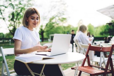 Neşeli ve iyimser kadın serbest çalışan sokak kafesinde açık dizüstü bilgisayarın önünde oturuyor ve sosyal medyada gülümserken mesajlaşıyor.