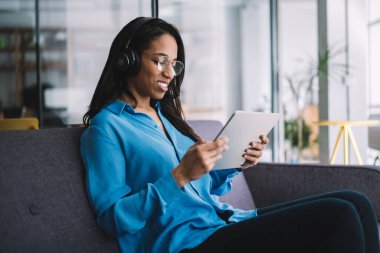 Kulaklık takmış, müzik dinleyen ve parmaklarını masaya koyup seçen Afro-Amerikan kadının yan görüntüsü.