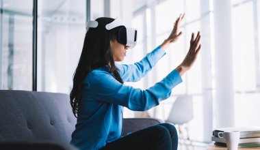 Mavi tişörtlü, uzun siyah saçlı bir kadının VR gözlük takıp sanal duvara dokunuşunun yan görüntüsü.