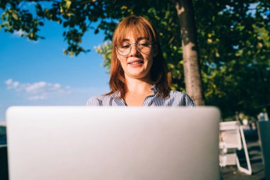 Başarılı Kafkasyalı serbest çalışan, dışarıda dizüstü bilgisayarla proje üzerinde çalışan, güneşli bir günde videolar izleyen ve iyi bağlantıların keyfini çıkaran pozitif hippi kız.