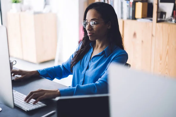 Hafif Gülüşlü Gözlüklü Mavi Gömlekli Afro Amerikalı Kadını Ofiste Oturuyor — Stok fotoğraf