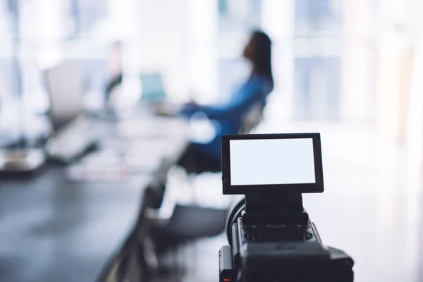 Modern video camera with empty white display placed in light open space office prepared for shooting worker on blurred background