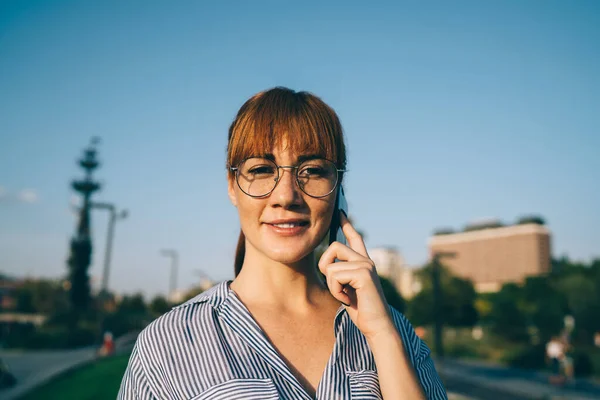 半長いですポートレートのRedhead女性で眼鏡楽しみ携帯電話スタンド上の通り 正ヒップスター女の子作る携帯電話コールでローミング見てでカメラ支出晴れた日に都市 — ストック写真