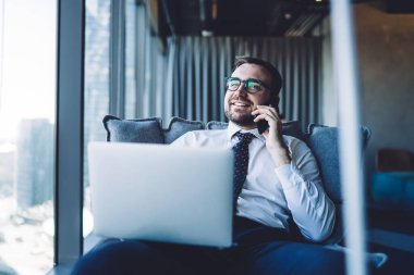 Optik gözlüklü mutlu işadamı bilgisayardaki online iş sırasında şirket bilgilerini tartışmak için akıllı telefon konuşması yapıyor, cep telefonu cihazıyla konuşan neşeli CEO.