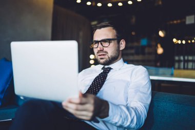 Optik gözlüklü, dijital dizüstü bilgisayardaki pazar ağı sırasında kurumsal finansal sorunları çözen kafası karışmış erkek girişimci, ticari web yatırımlarını kontrol eden şaşkın komisyoncu.