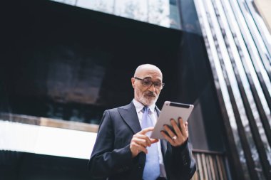 Resmi kıyafet ve gözlüklü kendinden emin kıdemli işadamından ve caddedeki ticari binanın önündeki beyaz sakallı tarayıcı tabletinden. 