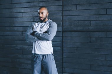 Yakışıklı, ciddi ciddi atletik Afrikalı, kel, sakallı, spor kıyafetli, kollarını çapraz yapıp, gri arka plana bakan yetişkin bir erkek.