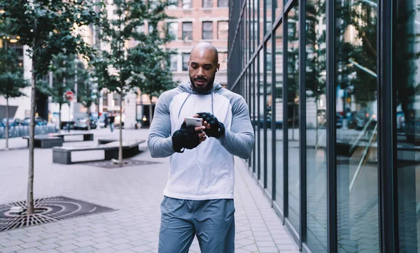 Lekkoatletyczny Łysy Brodaty Afroamerykański Sportowiec Słuchający Muzyki Słuchawkach Przeglądający Smartfony — Zdjęcie stockowe
