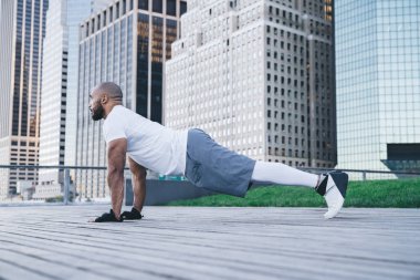 Kel sakallı Afro-Amerikan sporcu spor kıyafetleri içinde modern şehir merkezinin sokaklarında arka planda gökdelenler eşliğinde tahta gösterisi yapıyor.
