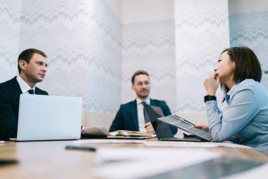 Ofisteki görüşmeler sırasında kağıt ve dizüstü bilgisayarlarla masaya otururken, şık giyinmiş, finansal raporların verilerini analiz eden yetişkin sakin girişimcilerden.