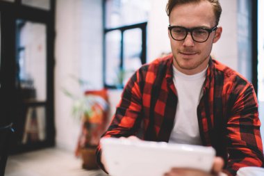 Günlük kıyafetleri ve gözlükleri olan genç bir erkek, kafeteryadaki akıllı telefondan arkadaşlarıyla konuşuyor.