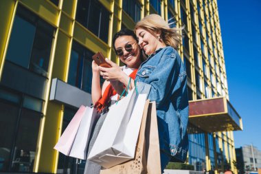 Neşeli bir kadın güneş gözlüklü, alışveriş merkezinin dışındaki akıllı telefon fotoğraflarına bakıyor.