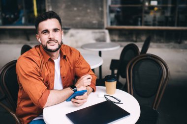 Mutlu ve neşeli bir adam kapalı dizüstü bilgisayarın önünde oturuyor ve sosyal medyaya bakıp gülümsüyor ve kameraya bakıyor.