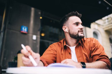 Düşük açılı, başarılı, sakallı, sıradan gömlekli hippi adam. Kafe 'de masa başında oturmuş gözlerini kaçırıyor.