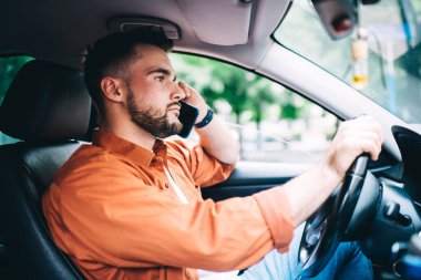 Pahalı bir arabada oturan ve arka planda akıllı telefondan konuşan günlük kıyafetli erkek sürücünün yan görüntüsü