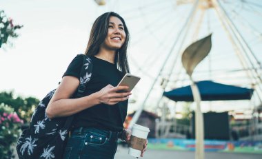 Mutlu hippi kız gezgin akıllı telefonuyla şehir festivaline giderken uygulama kullanıyor. Neşeli uluslararası kız öğrenci, eğlence parkında selüla tutarak tatilin tadını çıkarıyor.