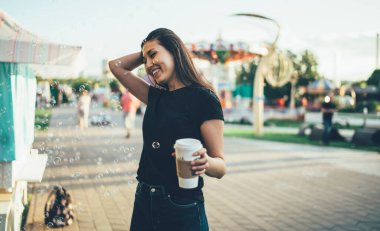 Gündelik giyinmiş mutlu Asyalı genç kadın elinde kahveyle şehir festivalinde tatil yaparken havada sabun köpüklerinin tadını çıkarıyor. Hafta sonu parkta eğlenen neşeli hippi kız.