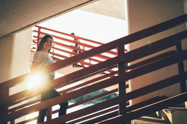 Mutlu neşeli Asyalı kız gündelik kıyafetleriyle boş zamanlarında merdivenlerde yürürken güneşli bir akşamüstü gülümseyen ve kameraya gülümseyen çekici genç kadın.