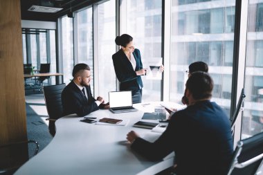 İş arkadaşlarına grafikler gösterirken ve ofiste projeyi tartışırken dizüstü bilgisayarın yanında duran resmi giysiler içindeki konsantre meslektaşlar