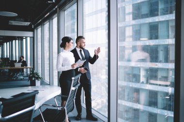 İş adamı ve camlı güzel bir kadın ofis koridorunda dikilip konuşurken camdan dışarı bakıyor.