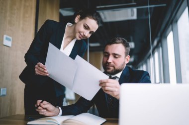 Aşağıdan memnun iş adamları resmi giysiler içinde açık modern ofiste toplantı sırasında masa başında kağıtlara konsantre oluyorlar.