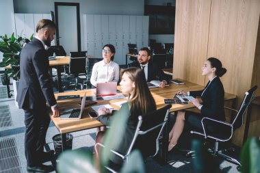 Modern bir CEO, modern bir konferansta çeşitli aletlerle masada dururken ofis çalışanlarına talimat veriyor.